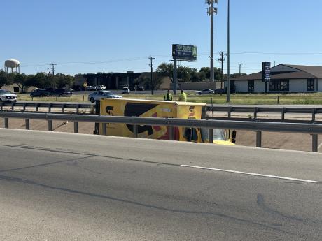 First responders assess the scene of a rollover involving a yellow delivery truck on W Loop 306. The vehicle, which had been flipped back onto its wheels, came to rest near a damaged guardrail. No injuries were reported.