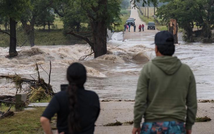 Onlookers gather on both sides as floodwaters swallow East Lane Valley Road in Comfort, Texas, on July 16, 2026. Heavy rainfall pushed the Guadalupe River out of its banks across the Hill Country.