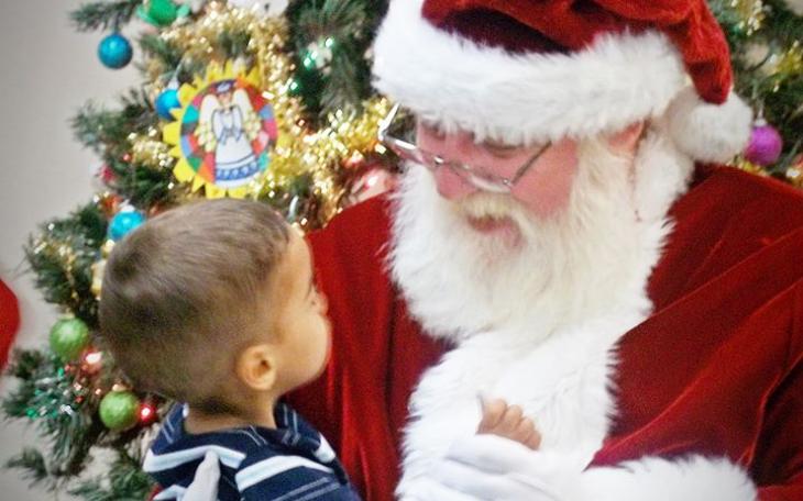 A little boy sits on Santa's lap at the Merry Little Christmas Party at Newbridge Family Shelter. (Photo courtesy of Sanford Mouton)