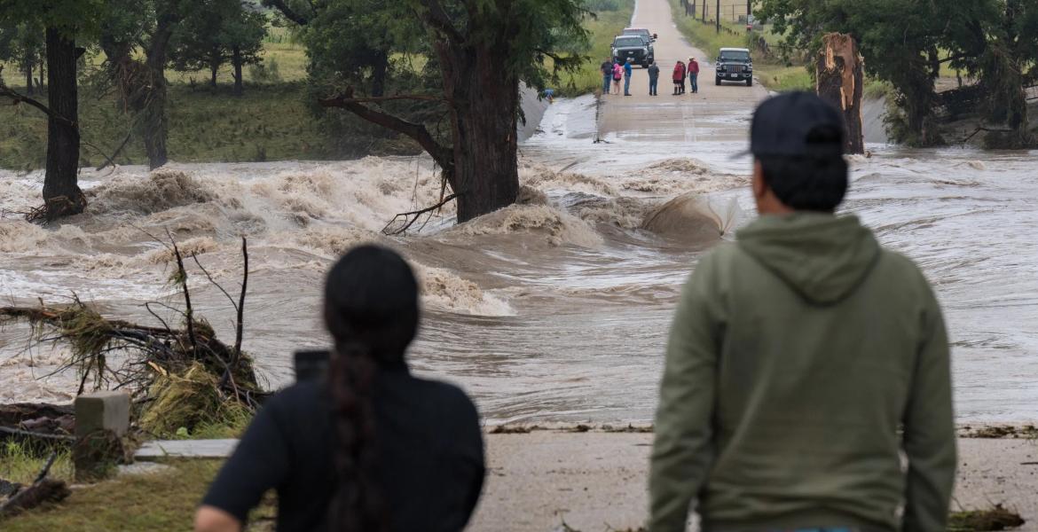 Onlookers gather on both sides as floodwaters swallow East Lane Valley Road in Comfort, Texas, on July 16, 2026. Heavy rainfall pushed the Guadalupe River out of its banks across the Hill Country.